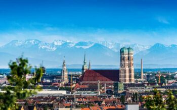 Eine Luftansicht auf die Stadt München. Im Hintergrund sind die Alpen zu sehen.