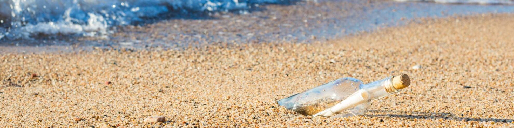 Eine Flaschenpost am Strand. Im Hintergrund das Meer