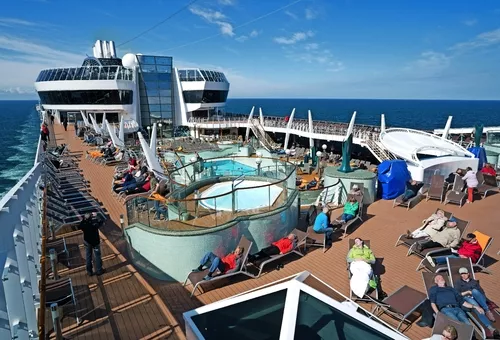 Menschen entspannen auf einem Kreuzfahrtschiffdeck mit Pool und Sonnenliegen.