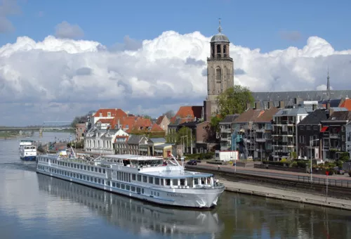 Passagierschiff MS Rigoletto auf einem Fluss vor einer Stadt mit Kirchturm.
