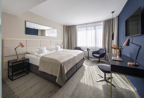 Modern eingerichtetes Hotelzimmer mit Doppelbett, Schreibtisch und Sessel.