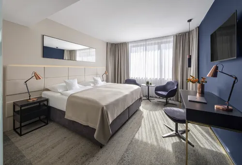 Modern eingerichtetes Hotelzimmer mit Doppelbett, Schreibtisch und Sessel.