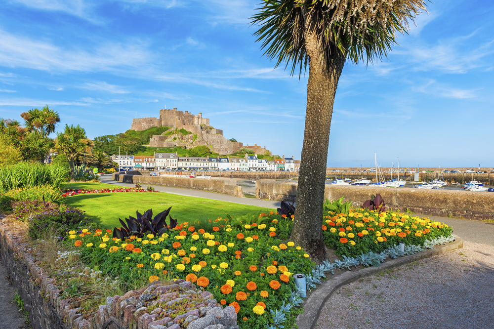 Blick über einen blühenden Park in Jersey mit Hafen und Küstenort im Hintergrund