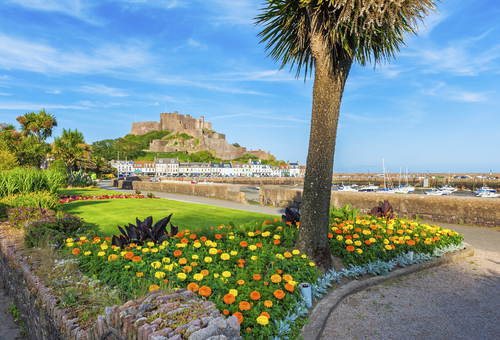Blick über einen blühenden Park in Jersey mit Hafen und Küstenort im Hintergrund