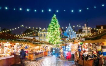 Beleuchteter Weihnachtsmarkt mit verschiedenen Ständen und einem großen Tannenbaum.
