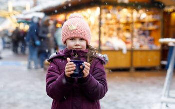 Ein Kind, das mit einer Tasse in der Hand auf einem Weihnachtsmarkt steht.