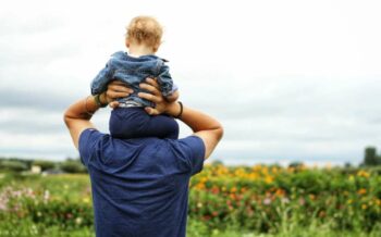 Vater mit einem Kind auf seinen Schultern. mit Blick auf ein Feld.