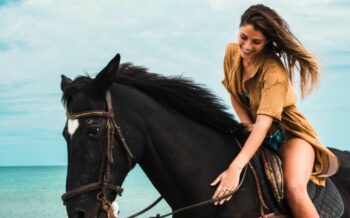 Frau sitzt auf einem Pferd am Strand.